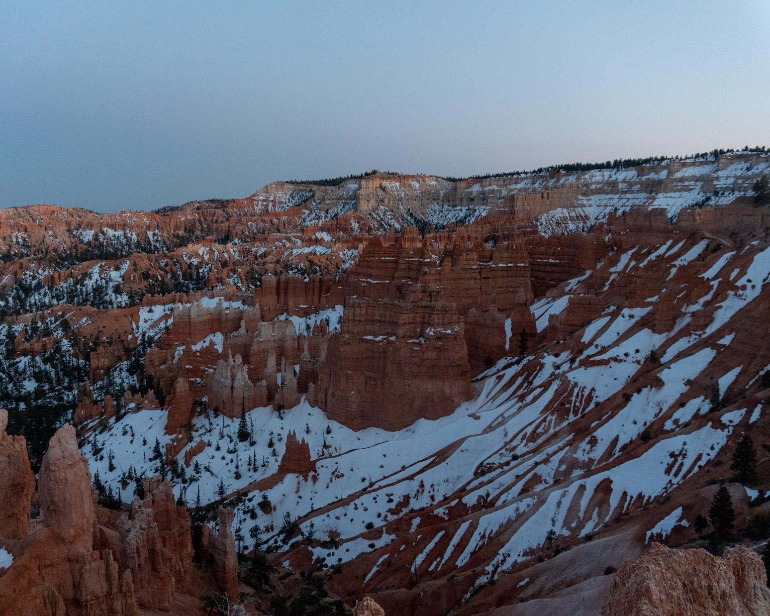 A view of an orange canyon and hoodoos partially covered with snow